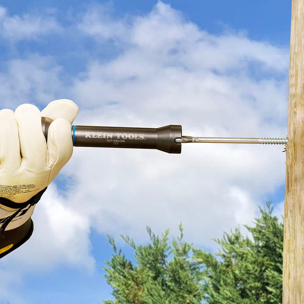 Gloved lineman using the side slot of the NRHD socket to drive a long screw-in hardware shaft directly into a wooden utility pole.