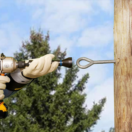 Utility technician in safety gloves aligning the side slot of an NRHD impact socket over an extended pole eyebolt aloft.