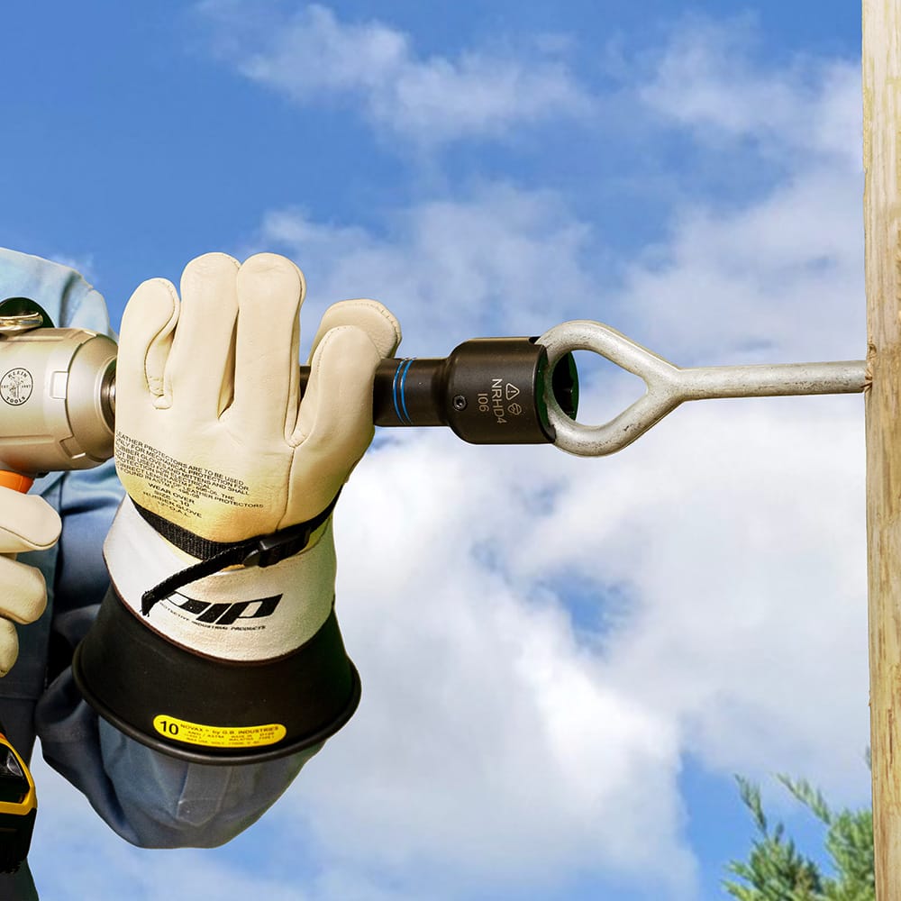 Utility worker in safety gloves turning a curved pole eyebolt using the NRHD4 slotted impact socket attached to a cordless driver.