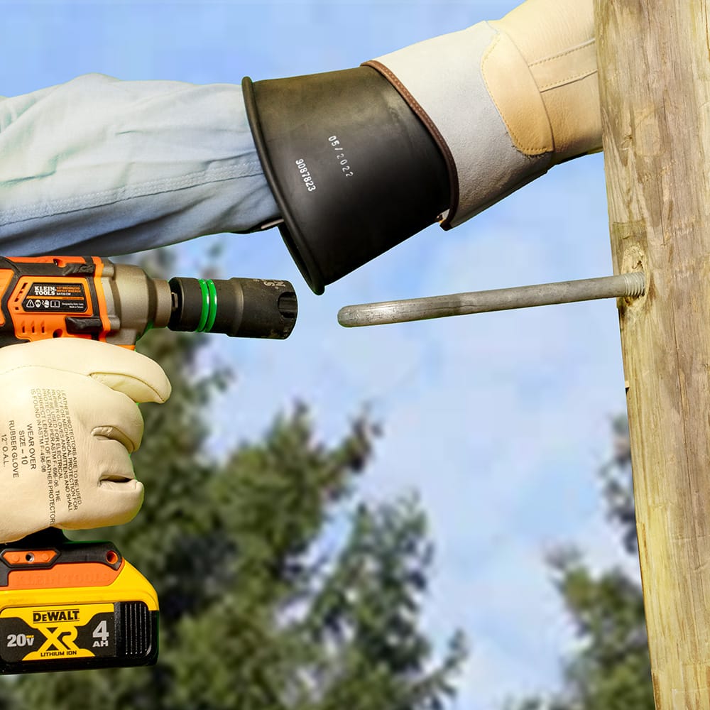 Line worker aligning a Klein side-slotted impact socket over a long utility pole J-bolt to demonstrate extended thread clearance.