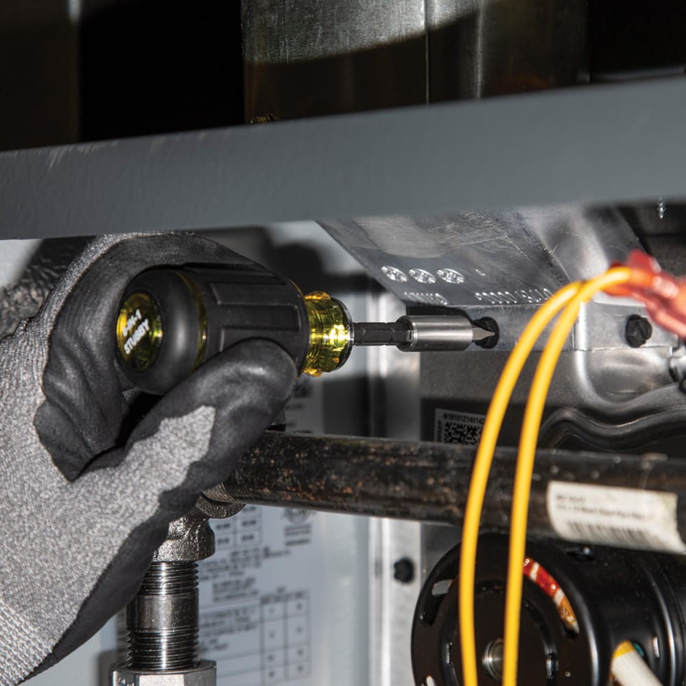 Technician using the Klein 32308HD stubby multi-bit driver to access and tighten screws in a cramped HVAC cabinet workspace.