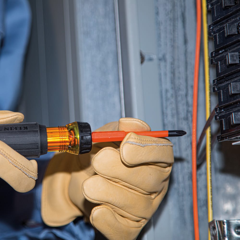 Electrician guiding the 1000V insulated #1 Phillips driver tip to safely tighten panel board wiring terminals near live conductors.