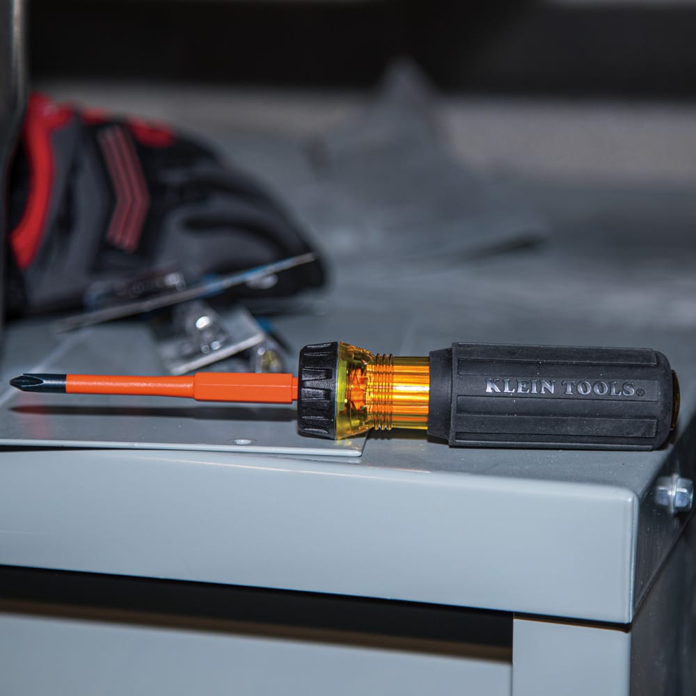Klein 32286 insulated 2-in-1 screwdriver resting on an electrical panel cabinet, showcasing its 1000V ASTM F1505 rated orange slim-tip shaft.