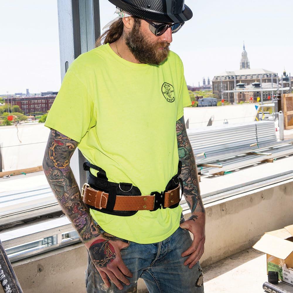 A worker wears the Klein Tools Ironworker Tool Belt System with the Pro-Pad and various leather tool holders while standing on a construction deck overlooking a cityscape.