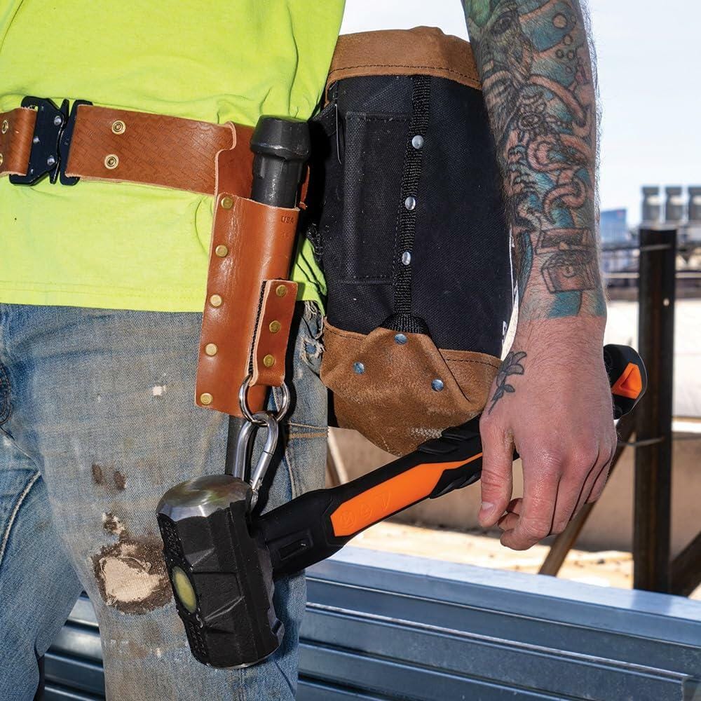 Close-up of the Klein Tools Ironworker Tool Belt System on a worker's hip, featuring the leather spud wrench holder and a flame-resistant bolt bag holding tools, including a tethered sledgehammer.