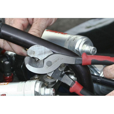 A detailed application photo showing the precision-ground shear blades of the Journeyman cable cutter as they engage a thick black cable, highlighting the high-leverage mechanical advantage and clinical accuracy of the tool.