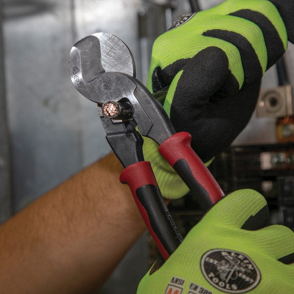 A focused action photo demonstrating the shearing power of the Klein J63225N cable cutter as it slices through a heavy-duty multi-strand copper cable in an industrial setting.