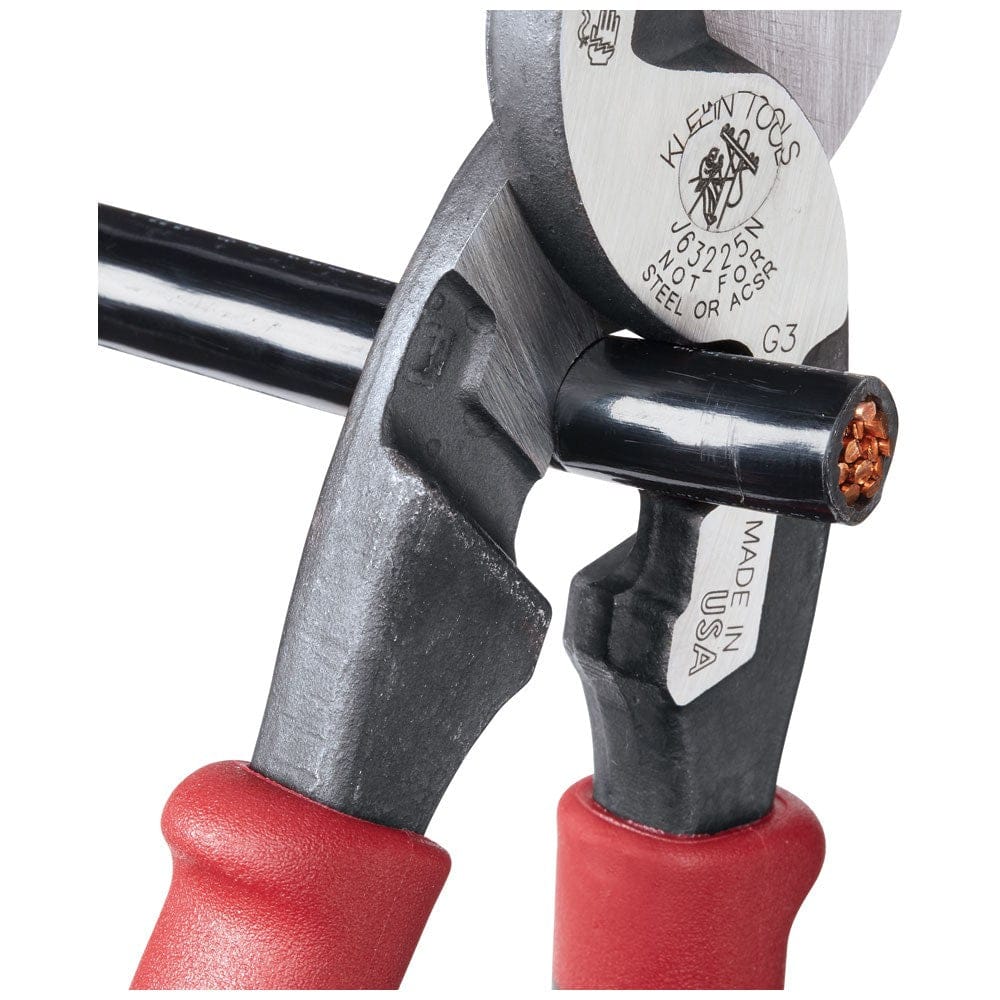 An action photograph of the Klein J63225N cable cutter performing a precise one-handed shear cut through a thick, black-insulated copper power cable.