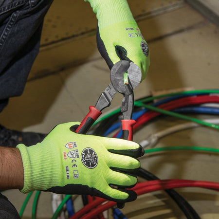 A close-up action shot of a professional wearing high-visibility safety gloves using the Klein J63225N Journeyman cutter to cleanly snip an insulated green grounding wire from a large bundle of cables.