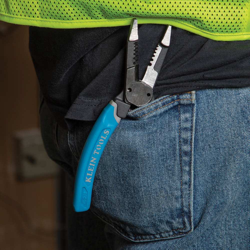 A lifestyle image showing the Klein K12035 forged wire stripper securely clipped onto the pocket of a tradesperson's blue jeans, demonstrating the tool's portability and accessibility on the job.