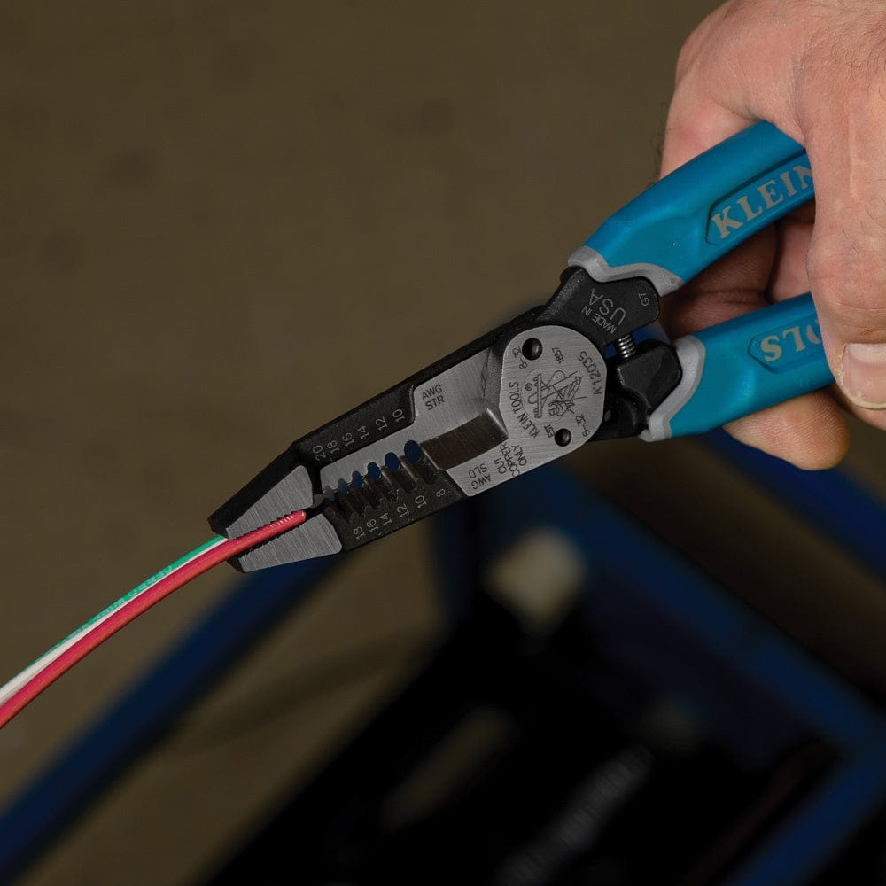 An action photograph of the Klein Tools K12035 wire stripper being used to precisely strip the insulation from a multi-conductor electrical cable, demonstrating the accuracy of the forged stripping holes.