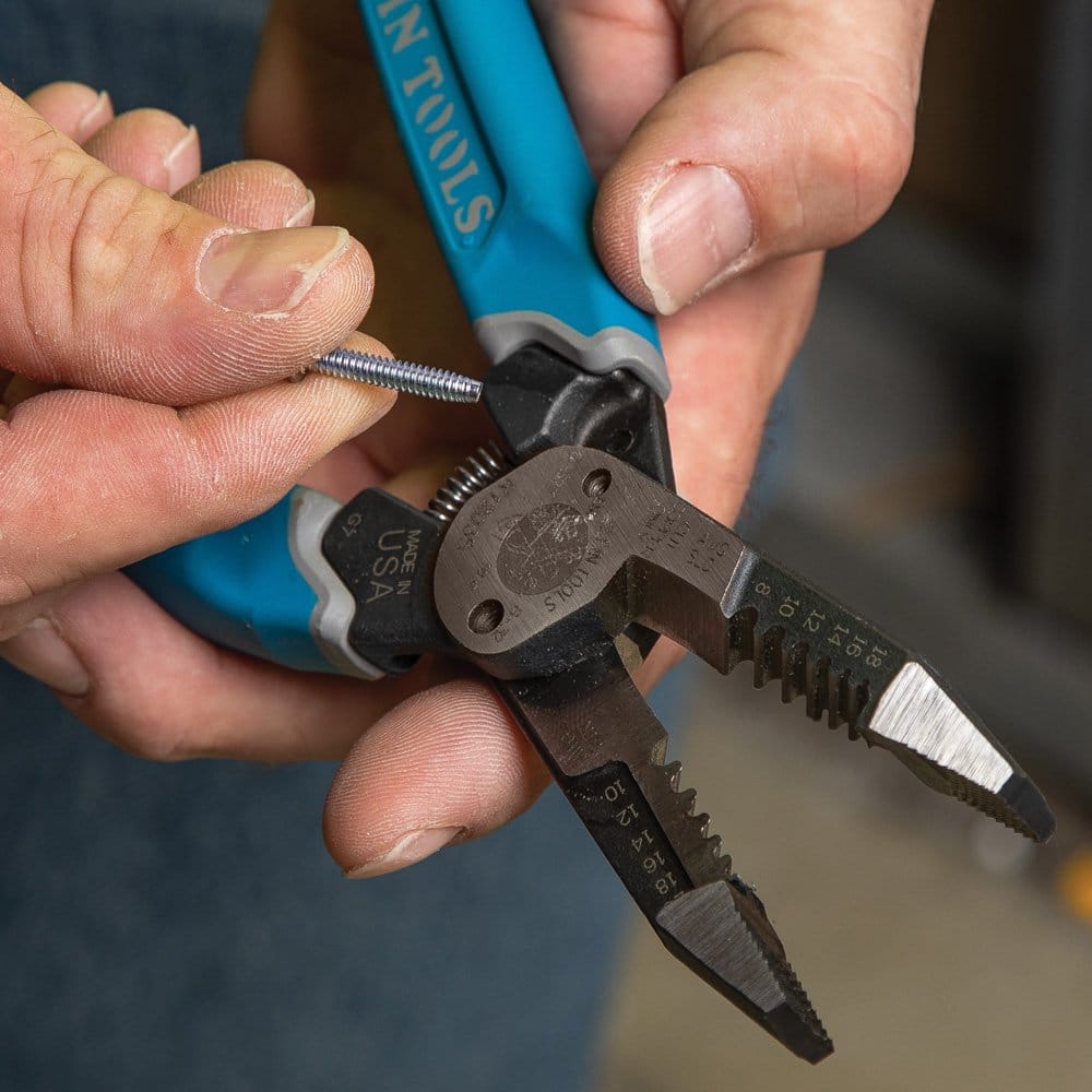A close-up view of a professional using the screw shearing feature on the Klein K12035 forged stripper to cleanly cut a silver machine screw without damaging the threads.