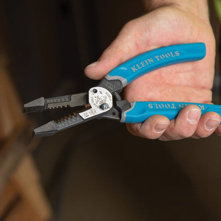 A hand holding the Klein K12035 wire stripper, showcasing the ergonomic Klein-Kurve handle design and the integrated hold-open spring that reduces hand fatigue during repetitive electrical work.