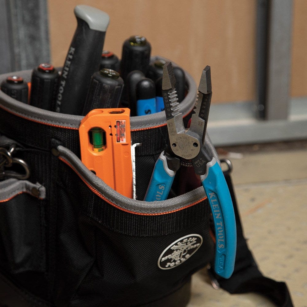 A professional black and orange tool pouch filled with various Klein Tools, with the K12035 heavy-duty forged wire stripper conveniently stored in a front pocket for easy access.