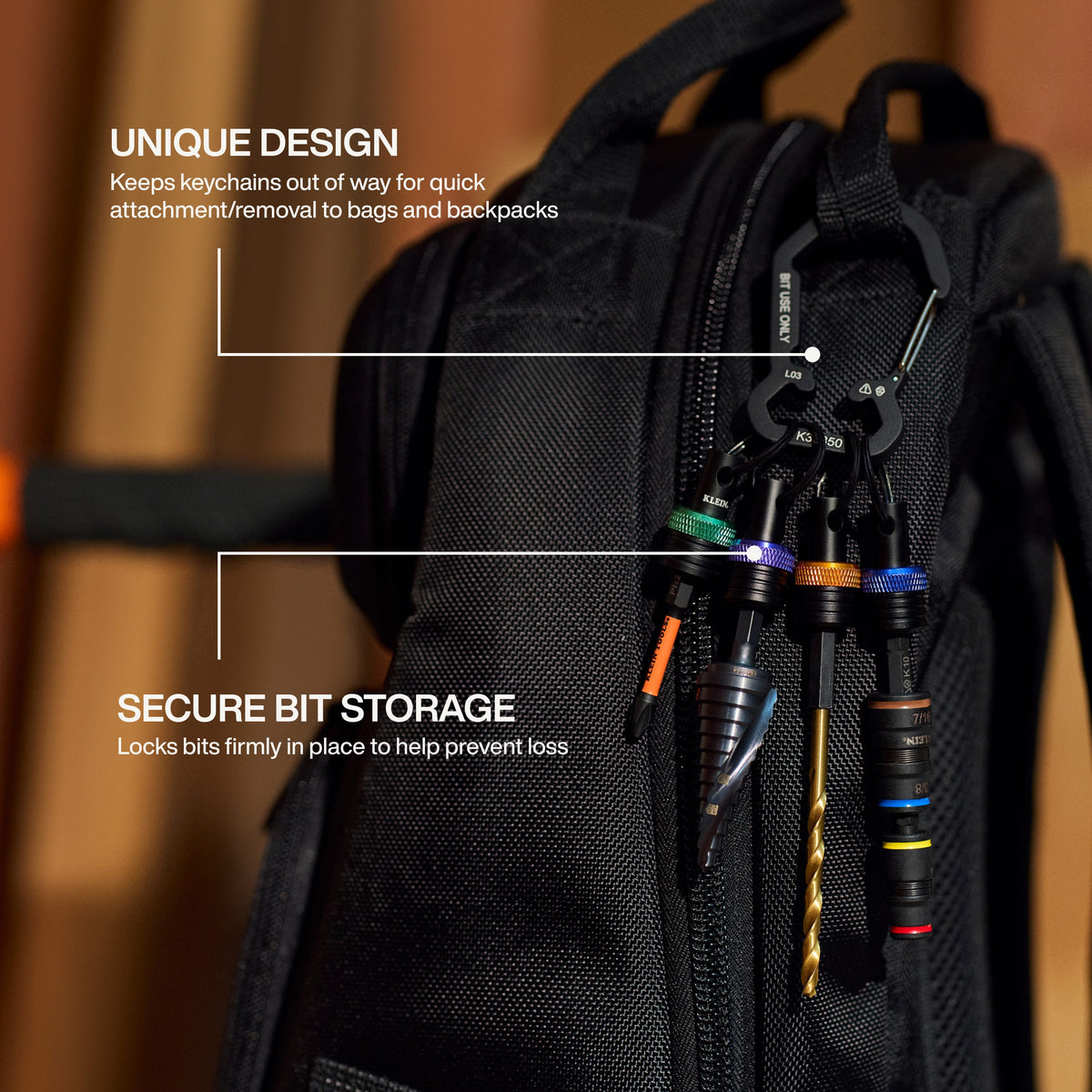 An in-use application shot showing the bit holder keychain set clipped to a black job site backpack, securely holding a Phillips bit, a step drill bit, a standard drill bit, and a flip socket to demonstrate hands-free storage and loss prevention.
