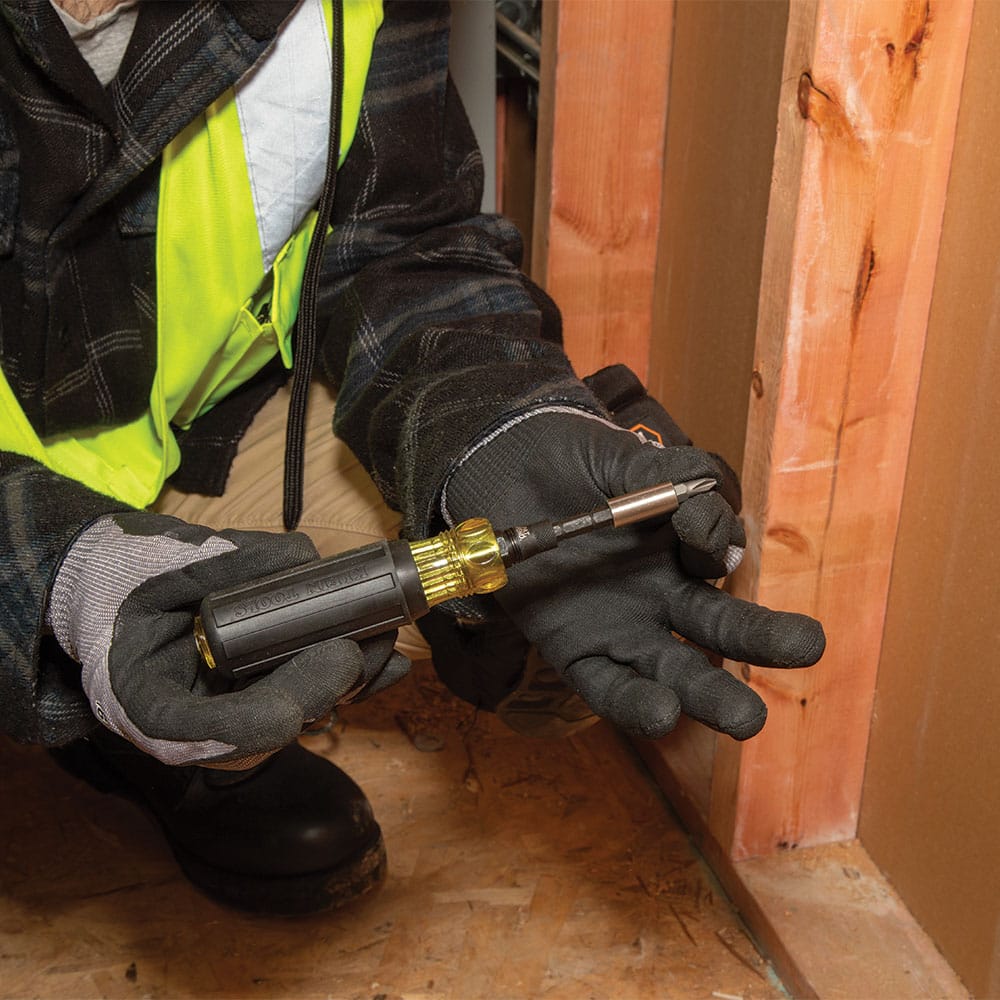 Technician holding the Klein Cushion-Grip screwdriver assembly next to a wall stud and an open MODbox bit case.