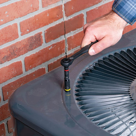Technician using a Klein ratchet fitted with a 32501HD KNECT 1/4-inch and 5/16-inch nut driver to service an outdoor HVAC condenser unit.