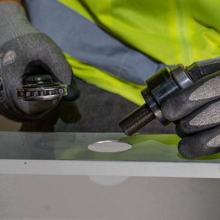 A worker holds the two halves of the knockout punch, showing the clean hole created in a metal panel and the split slug in the die.