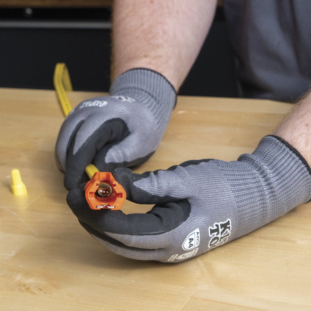 A close-up of gloved hands holding the orange multi-tool to display the end socket containing a red wire nut, demonstrating its use as a nut driver.