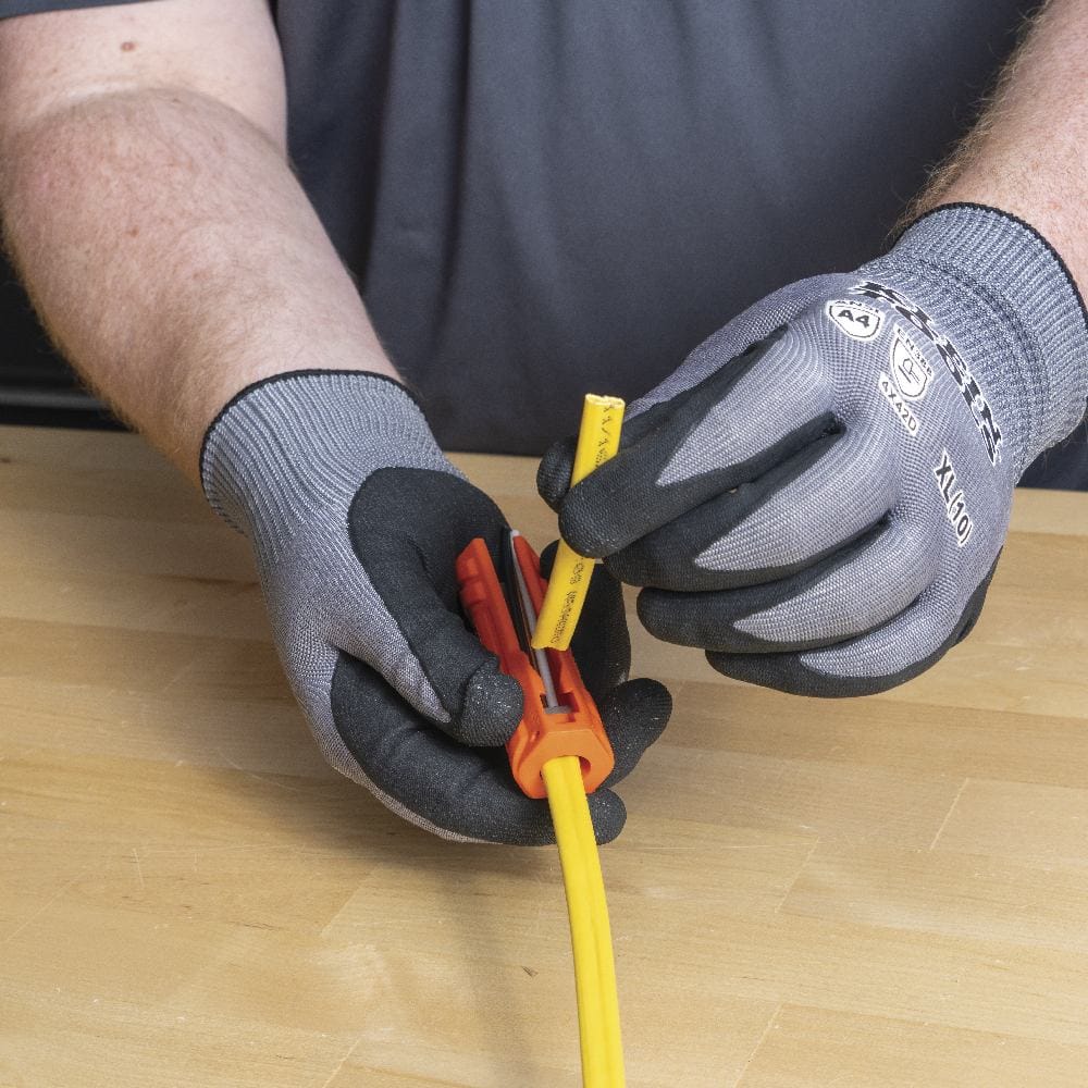 Gloved hands sliding the orange multi-tool along the yellow NM cable to slice the outer sheath using the internal ripping blade.