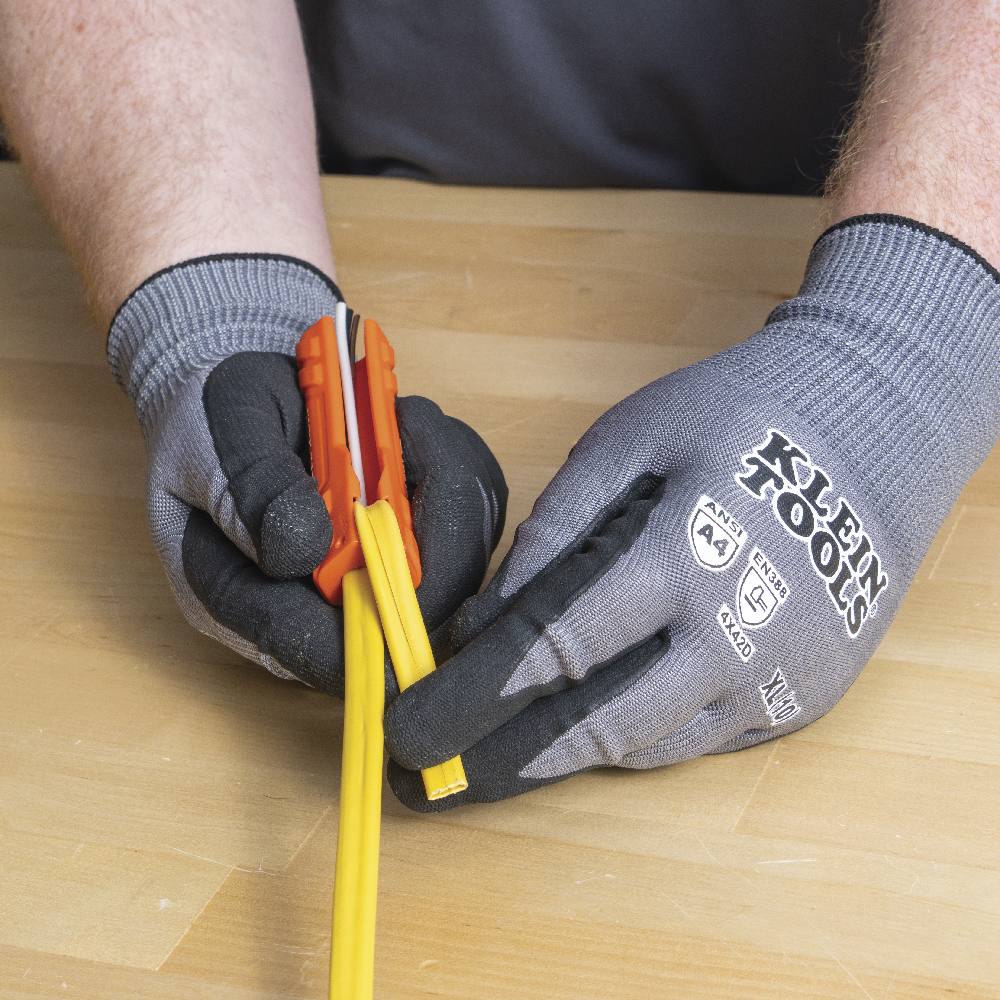 Gloved hands separating the sliced outer jacket of the yellow NM cable to reveal the insulated conductors and ground wire inside.