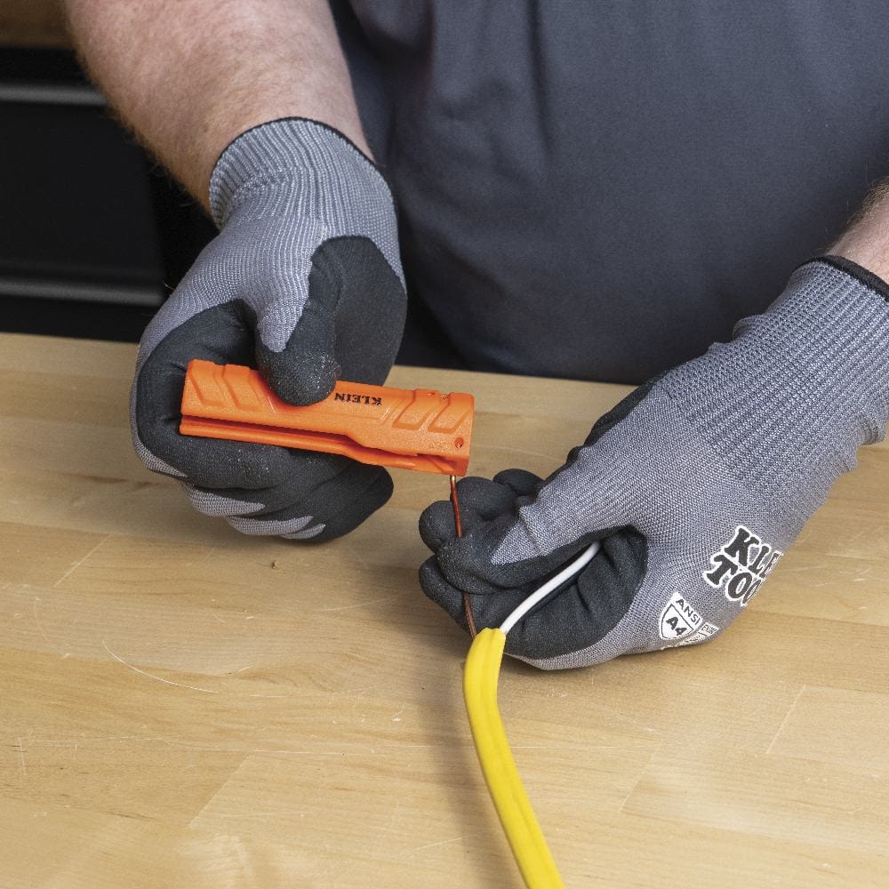 Gloved hands inserting a bare copper wire into the designated "LOOP" hole on the side of the orange multi-tool.