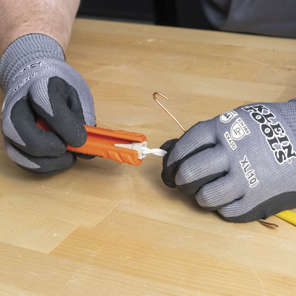 Gloved hands using the hollow end of the orange multi-tool to twist a wire nut onto a pair of white wires securely.