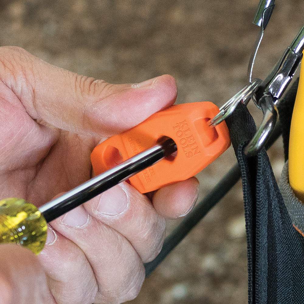 A close-up action shot of a person's hands using the MAG2 tool, which is attached to a tool bag, to magnetize a yellow-handled screwdriver by sliding the metal shaft through the center hole.