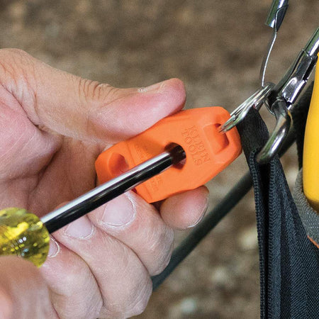 A close-up action shot of a person's hands using the MAG2 tool, which is attached to a tool bag, to magnetize a yellow-handled screwdriver by sliding the metal shaft through the center hole.