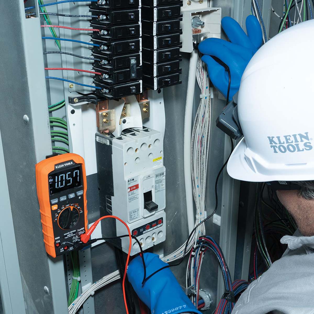 Person wearing a hard hat and gloves working on electrical panel with a multimeter