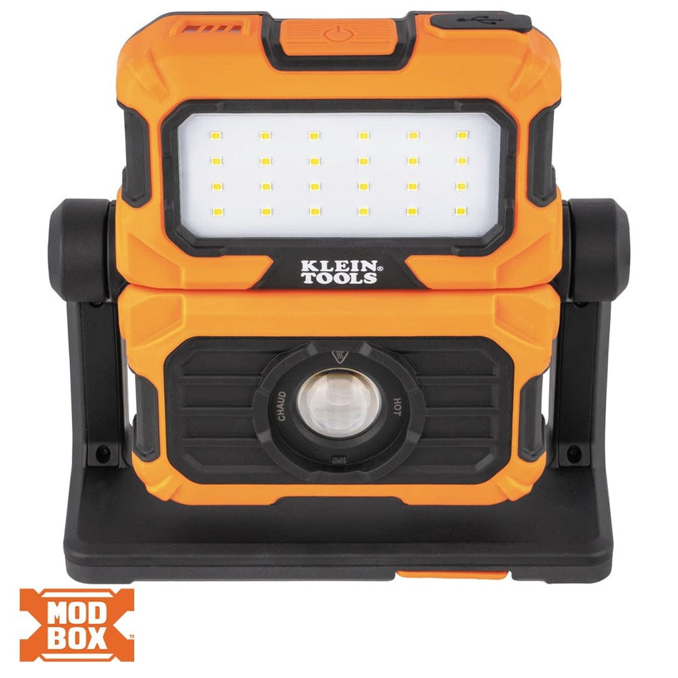 Front view of the orange and black Klein Tools 56417 MODbox rechargeable work light. The dual-beam design features a top LED flood light panel and a bottom high-intensity spot light lens, housed in a rugged, impact-resistant body for demanding jobsite environments.