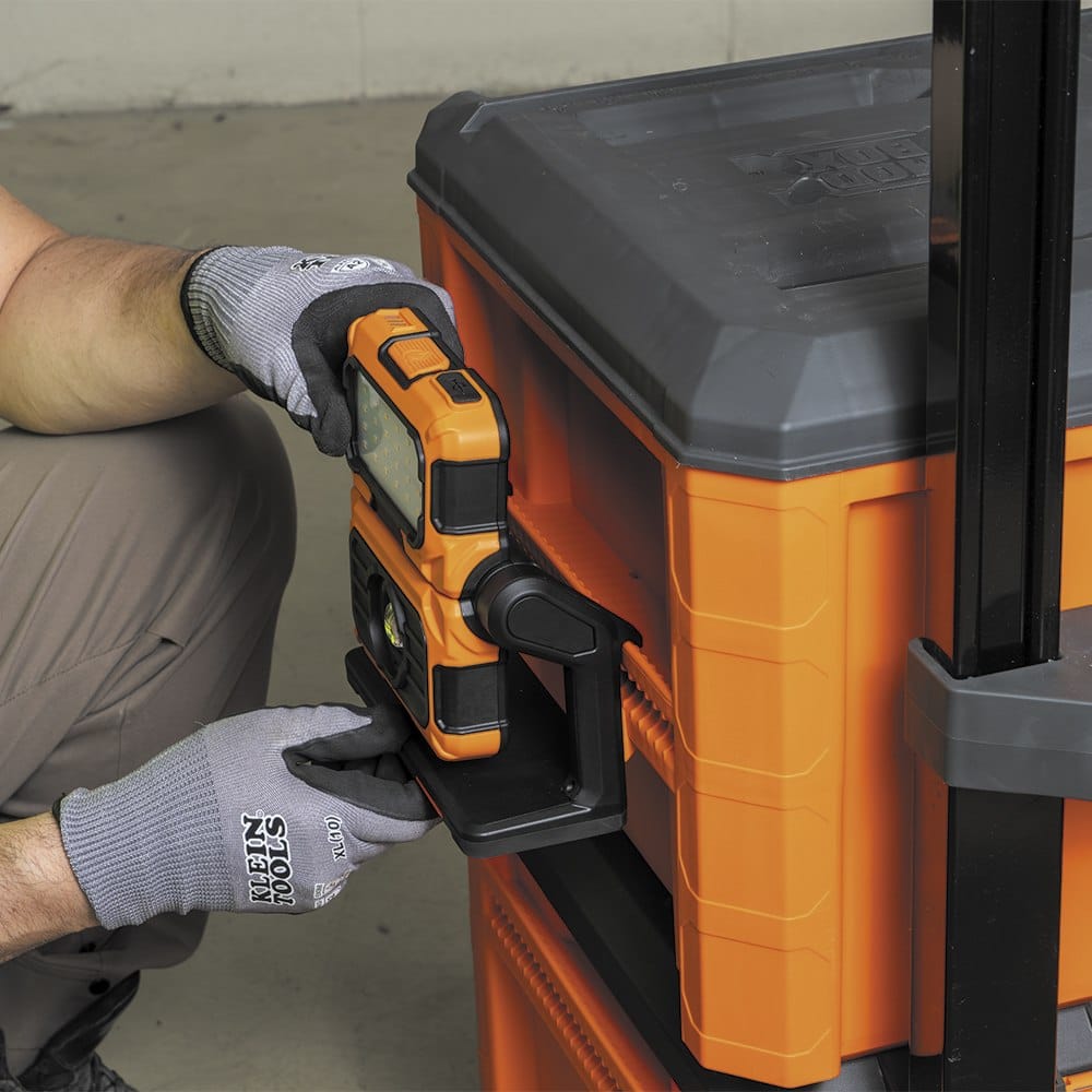 Side-angle view of the MODbox work light fully seated on the mounting rail of an orange tool box. The design ensures the light remains accessible and securely attached during transport across rough jobsite terrain.