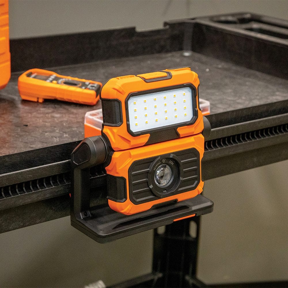 Front-facing view of the 56417 LED light resting on a workbench alongside a digital multimeter and small parts container. This highlights the tool's compact footprint and utility as a standalone floodlight for technicians and hobbyists.