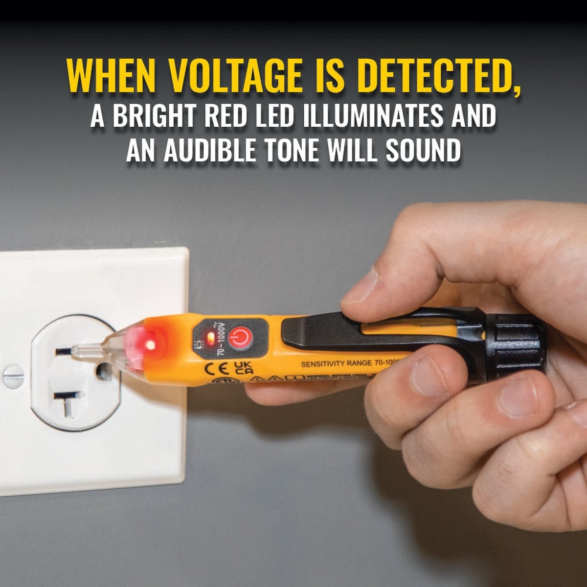 Action shot showing the NCVT-1XT waterproof non-contact voltage tester checking a standard wall outlet. The clear tip is illuminated with a bright red LED, signifying live voltage detection, while the technician holds the tool securely using the integrated black pocket clip area.