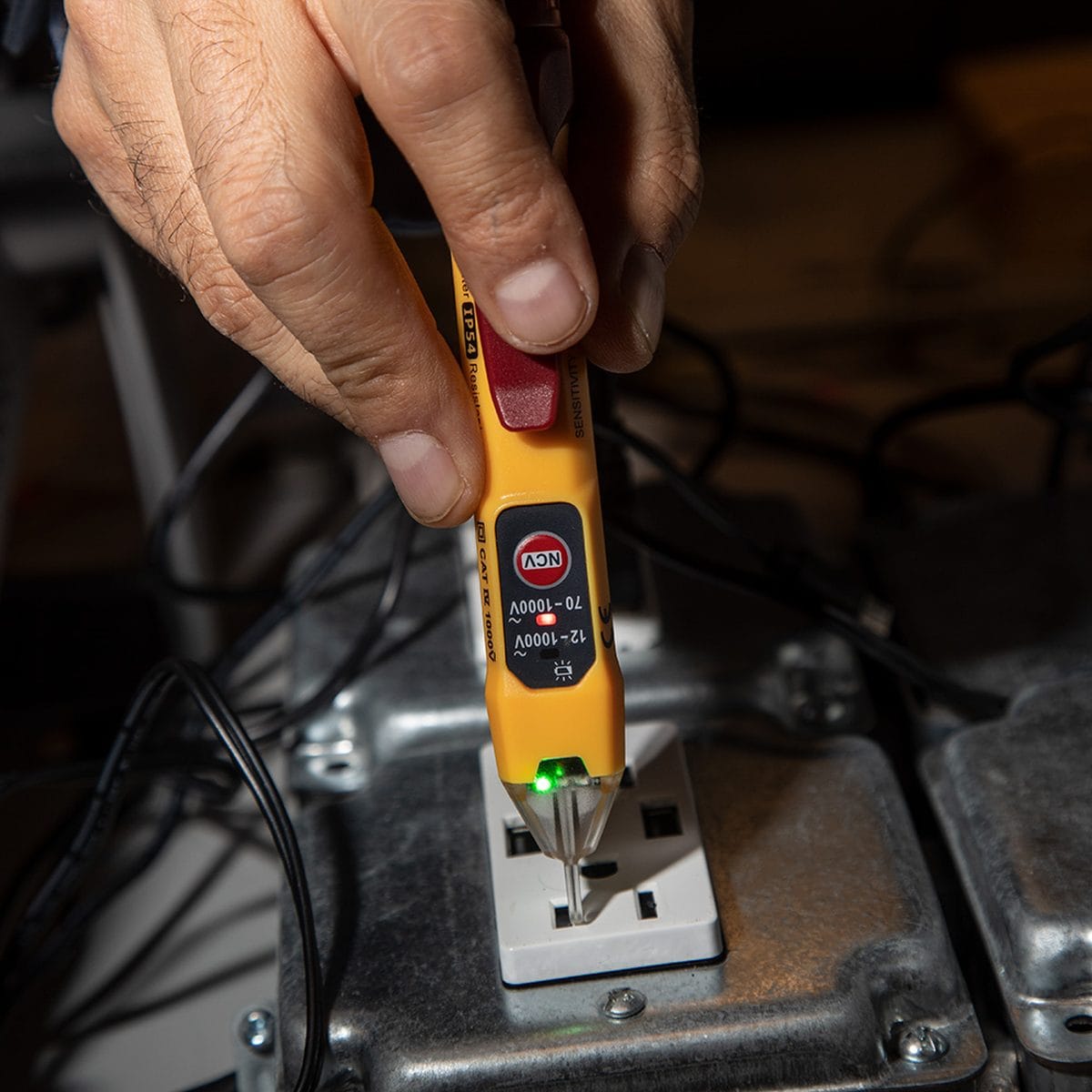 Action shot of a technician using the NCVT-2P dual-range tester to verify power at a residential wall receptacle. The clear tip is illuminated with a red LED indicator, providing a simultaneous visual alarm that live AC voltage is present in the circuit.