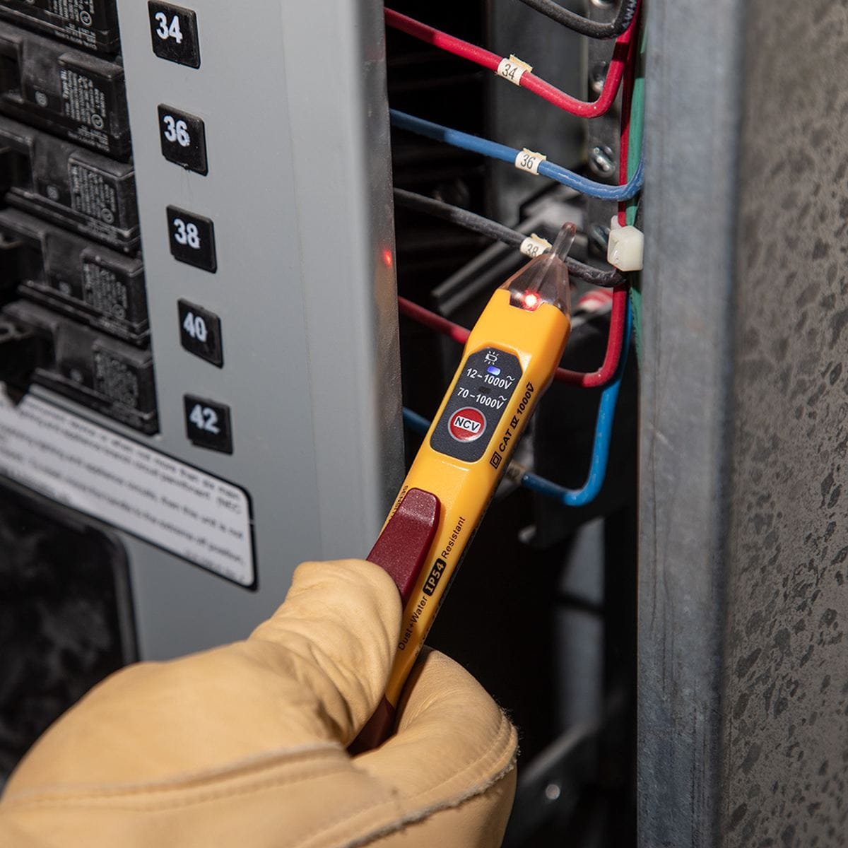 Hand wearing a glove holding a voltage tester near electrical panels.