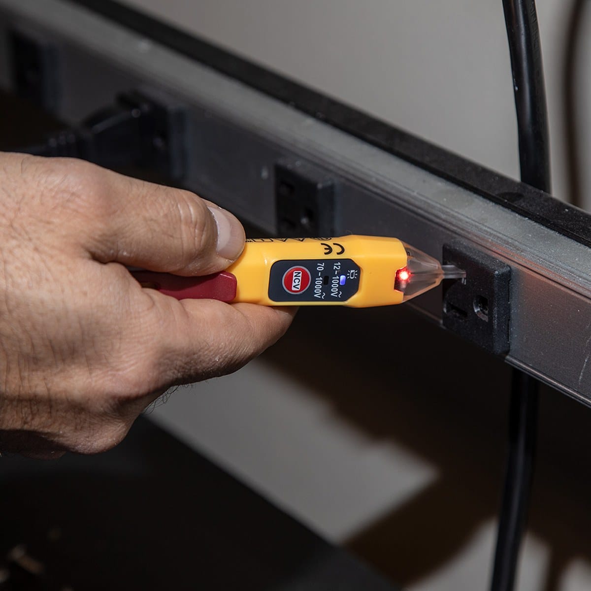 Hand using a yellow electrical tester to check for electricity on a wall socket.