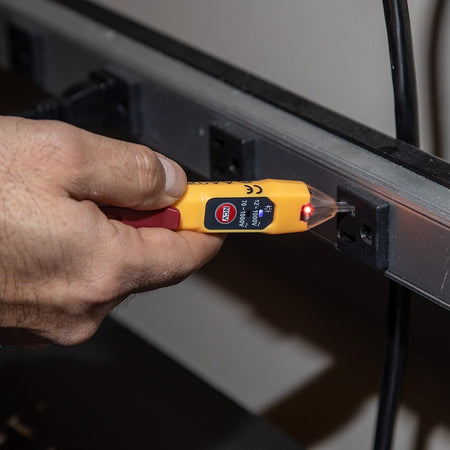 Hand using a yellow electrical tester to check for electricity on a wall socket.