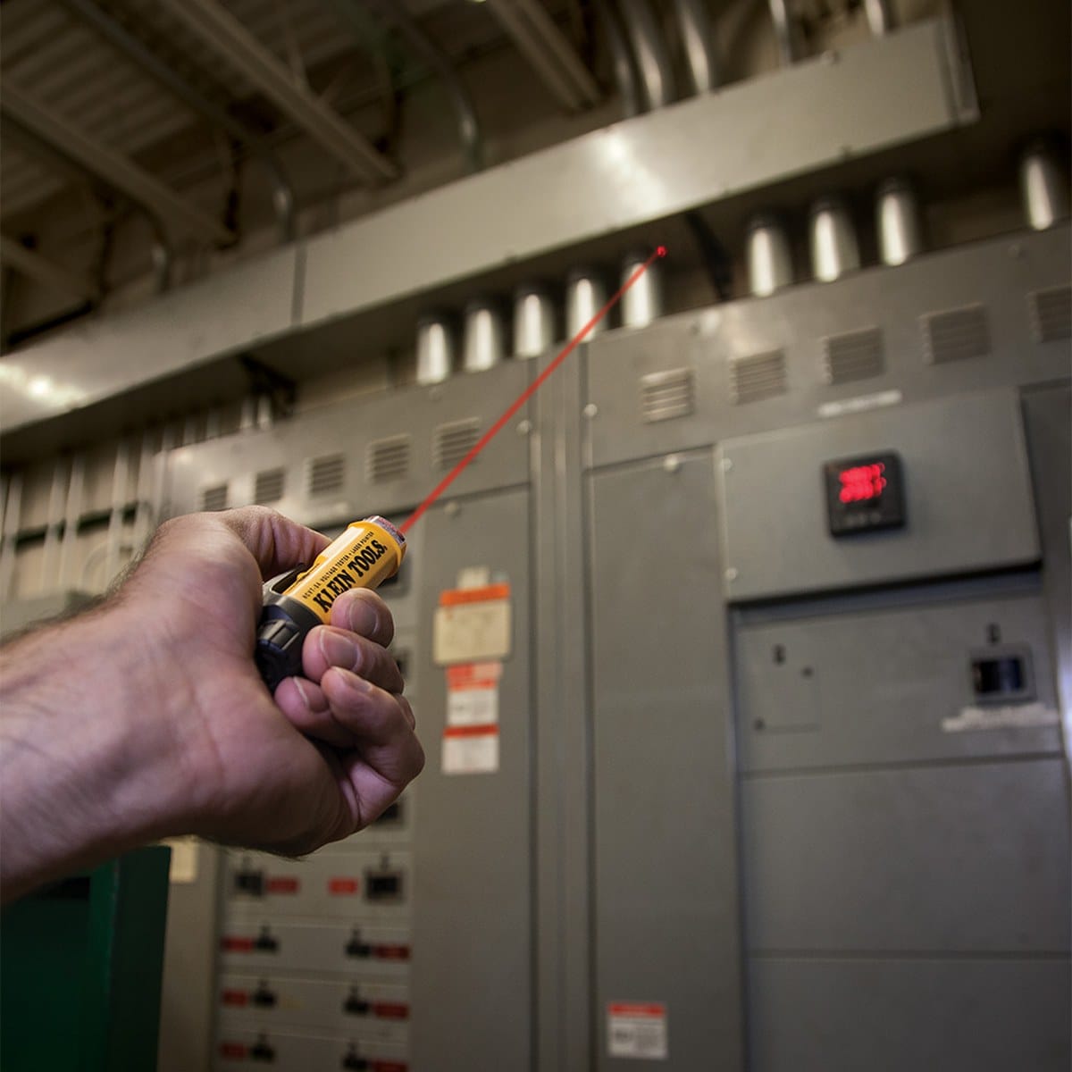 A professional application shot of a technician using the NCVT5A laser pointer to identify a specific breaker on a large industrial power distribution panel. The image highlights how the laser pointer aids in communication and identification on complex jobsites.