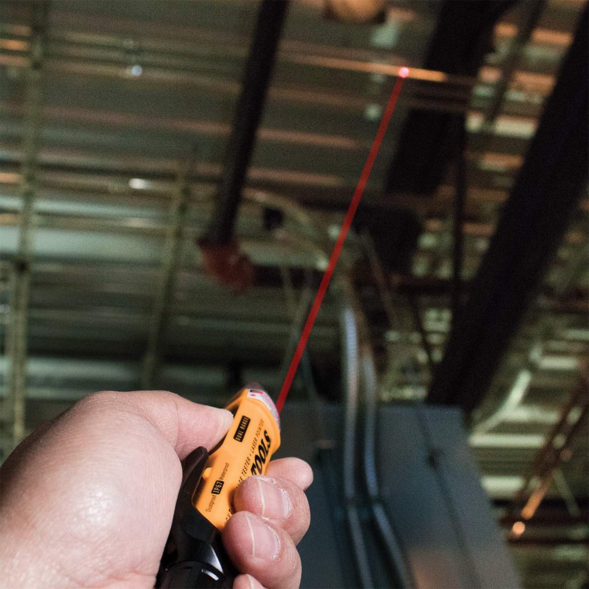 The NCVT-5A being used to trace an overhead electrical run in a high-ceiling industrial environment. The bright red integrated laser pointer is projected onto a distant conduit, showcasing the tool's utility for identifying specific components or marking distances on the jobsite.