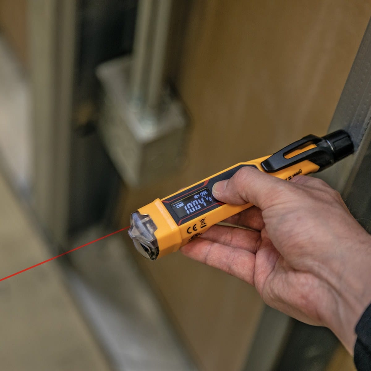 The NCVT6 laser distance meter being used to measure a wire run in a commercial building. The red laser beam is projected toward a distant wall while the technician views the precise measurement on the backlit reverse-contrast LCD.