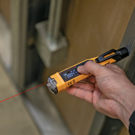The NCVT6 laser distance meter being used to measure a wire run in a commercial building. The red laser beam is projected toward a distant wall while the technician views the precise measurement on the backlit reverse-contrast LCD.