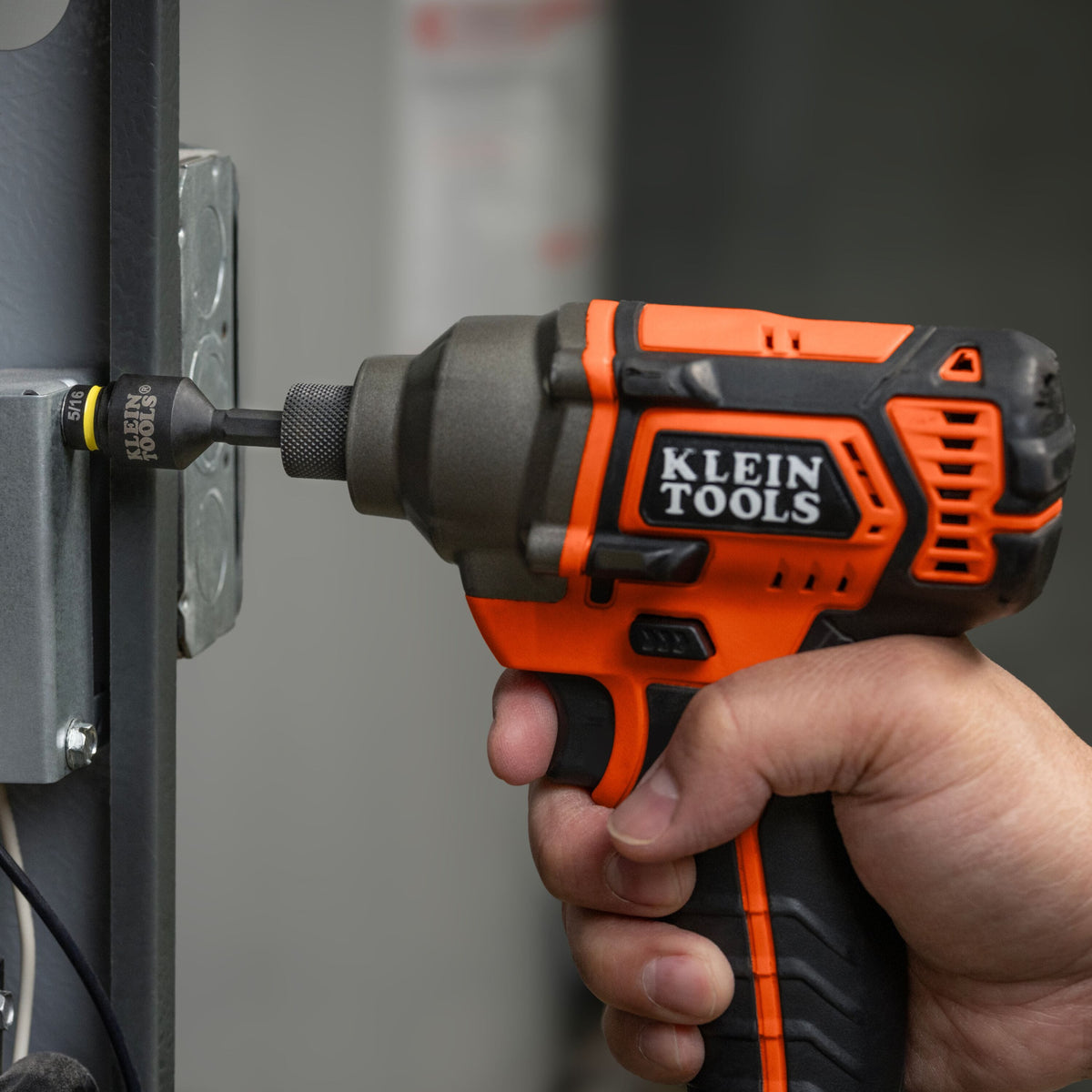 Electrician using a 1/4-inch impact driver with a Klein 5/16-inch socket to rapidly secure a metal electrical box panel screw.
