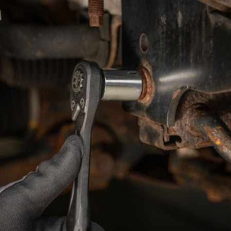Mechanic using the low-profile Klein pass-through ratchet and a standard socket adapter to loosen a tight chassis bolt in a cramped bay.