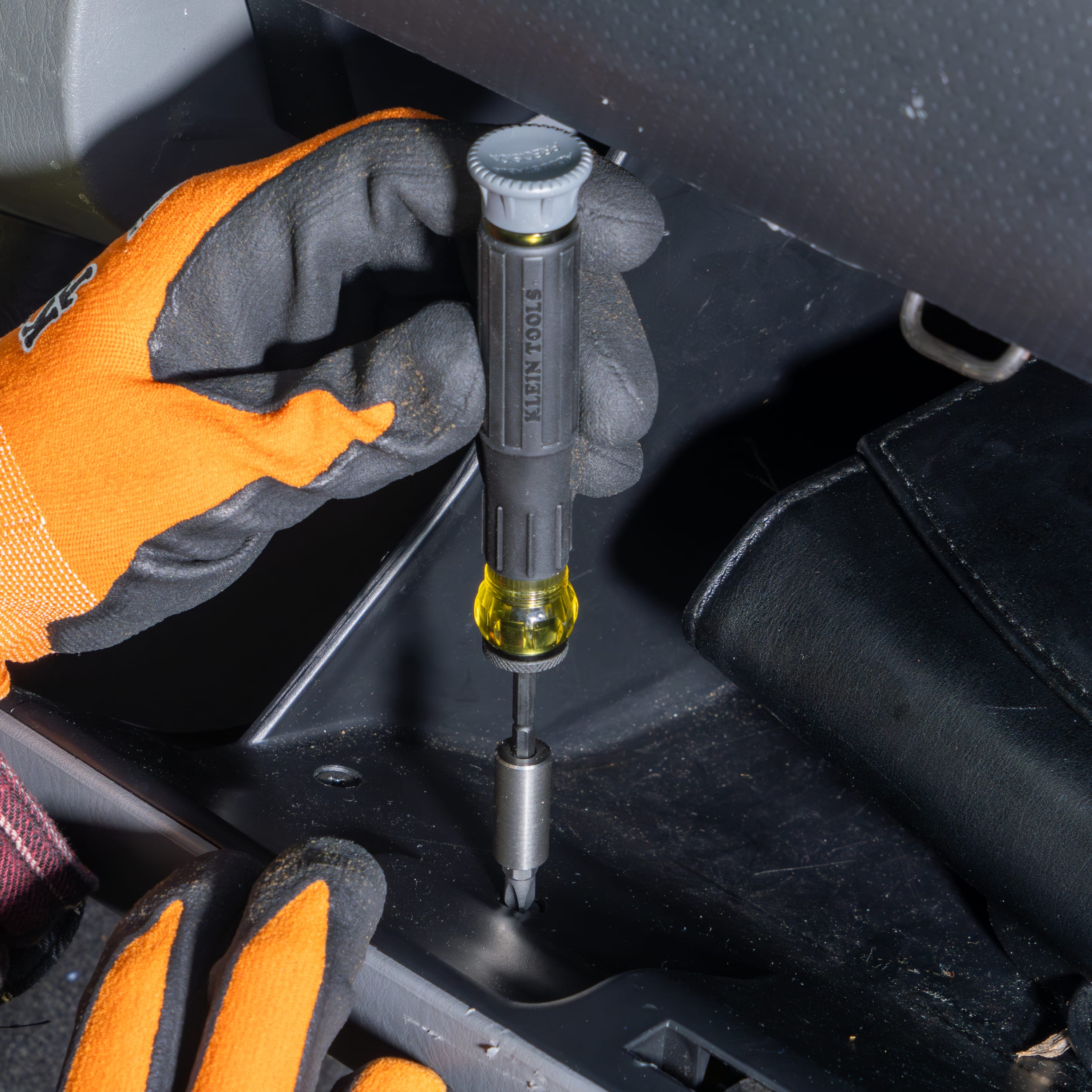 Technician using the Klein 32787 precision screwdriver with a nut driver attachment to secure a fastener inside a vehicle glove box.