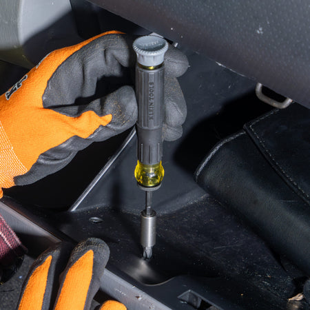 Technician using the Klein 32787 precision screwdriver with a nut driver attachment to secure a fastener inside a vehicle glove box.