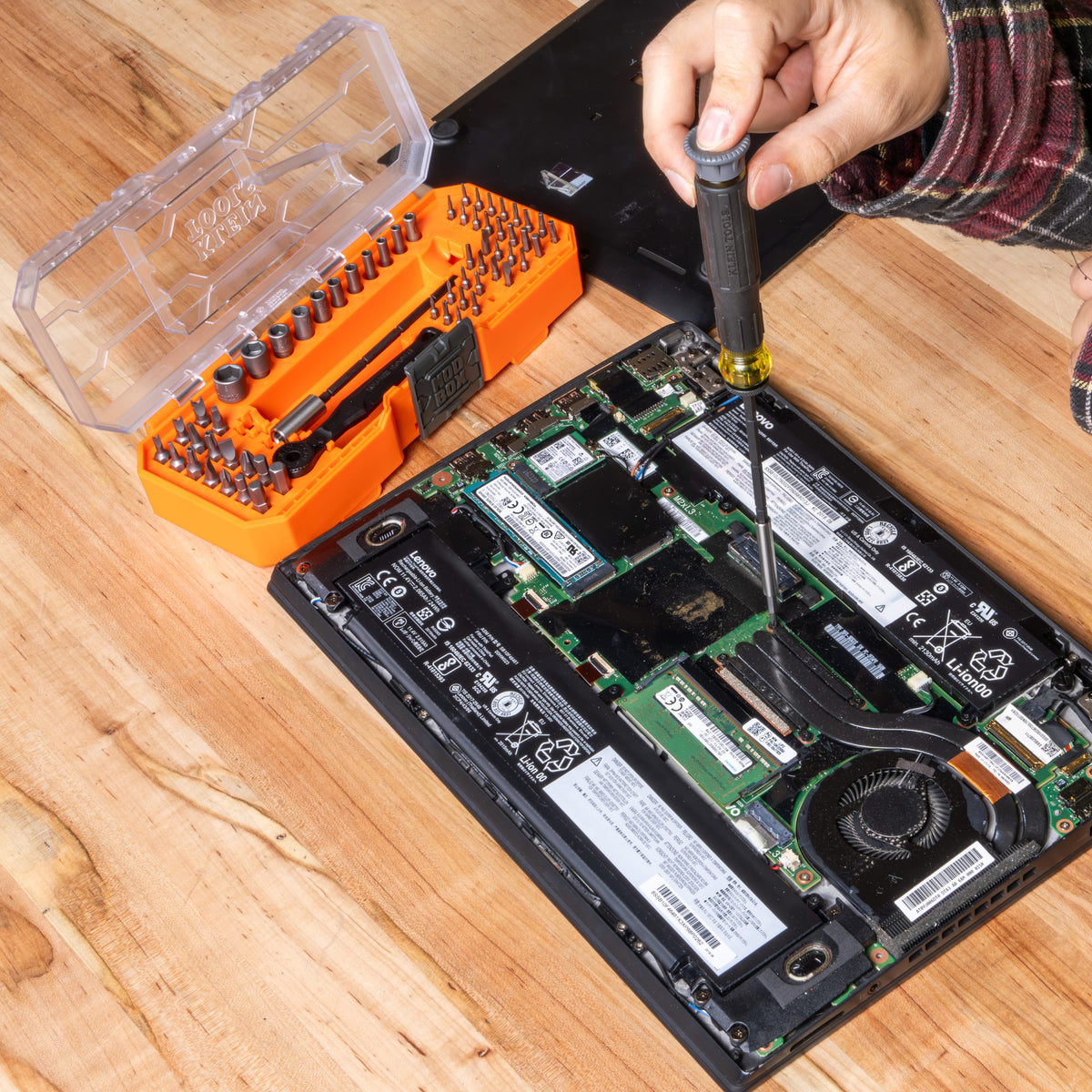 Technician using the precision spin cap screwdriver to fasten micro-screws inside an open laptop computer assembly.