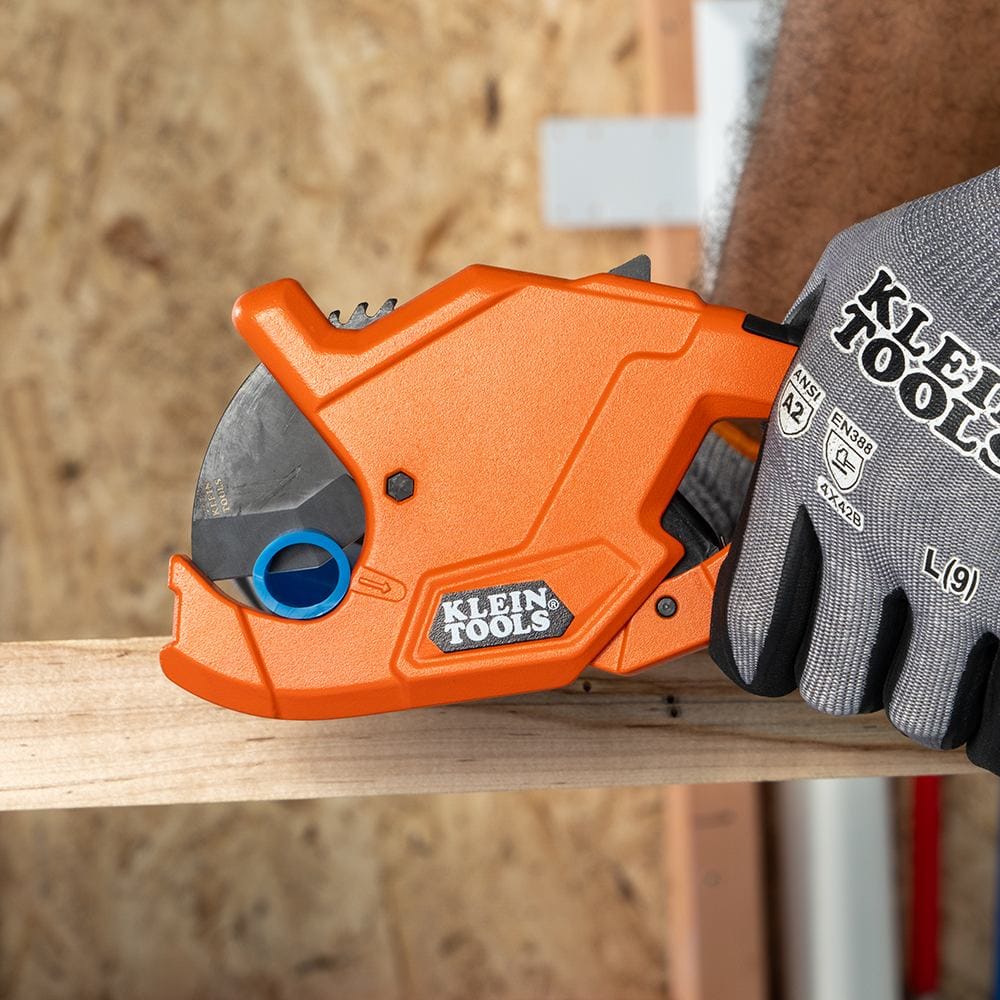 Close-up of the Klein Tools 50044 heavy-duty pipe cutter being used on a blue PEX tube. The image emphasizes the secure fit of the pipe in the lower jaw and the alignment of the precision blade, ensuring a burr-free finish for plumbing installations.