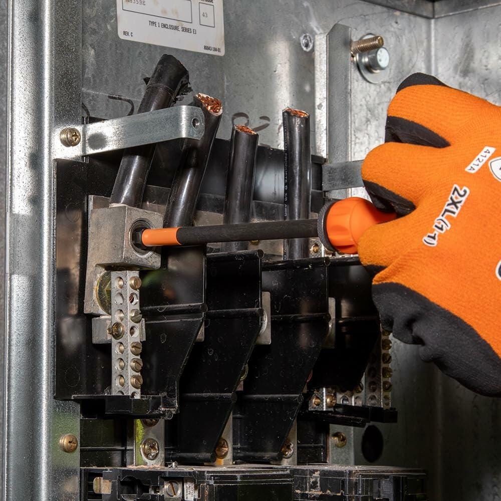A worker wearing an orange and black glove uses the Klein Tools T-Handle bit set with a long bit to secure a terminal connection inside an electrical enclosure.