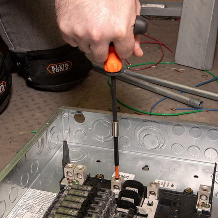 A tradesperson uses the Klein Tools Ratcheting T-Handle with an extended bit to drive a screw inside a deep metal electrical panel box.